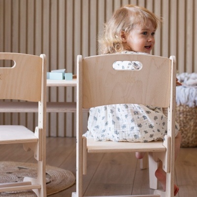 Criança sentada numa cadeira infantil de madeira clara com texto 'baby Dood' nas costas.