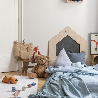 Quarto infantil com cama baixa azul, ursinho, candeeiro de dinossauros e prateleira em forma de casa