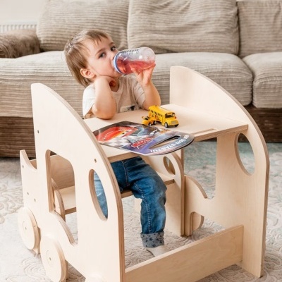 Criança numa secretária de madeira em formato de carrinho com brinquedos e sofá ao fundo