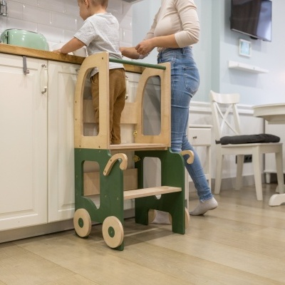 Criança numa escada verde e madeira clara a ajudar na cozinha com mulher ao lado