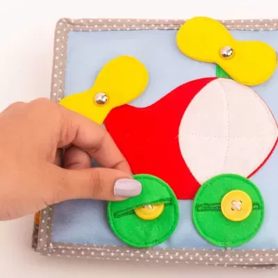 Puzzle infantil de tecido colorido com peças em feltro e botões, vermelho, amarelo, verde e azul.