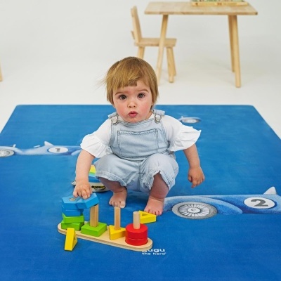 Criança sentada a brincar num tapete azul com padrão de aviões e números.