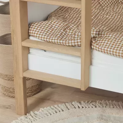 Cama de madeira clara com lençol xadrez e tapete redondo bege