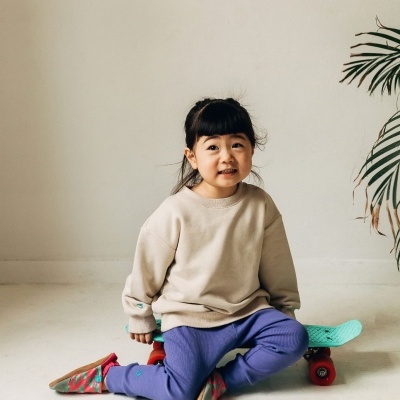 Criança com roupa casual e skate no chão em ambiente interior simples