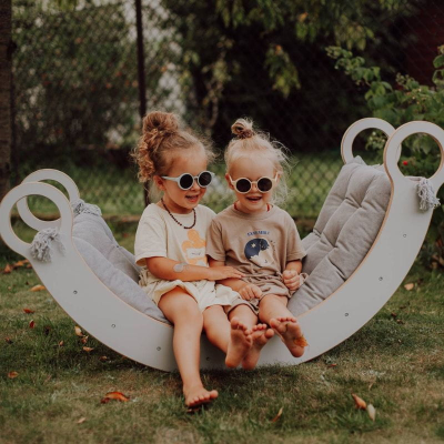 Duas crianças sentadas numa cadeira baloiço branca acolchoada no jardim