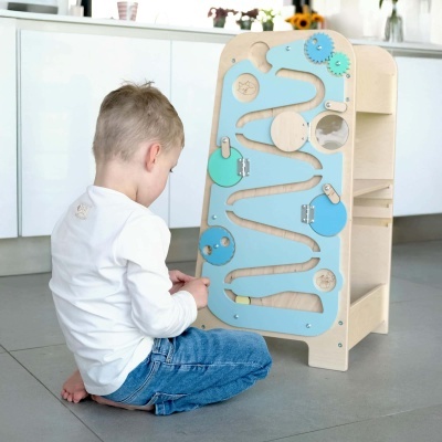 Brinquedo educativo de madeira com painel azul claro e engrenagens, criança brincando no chão