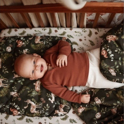 Bebé numa cama com roupa de cama de padrões de floresta numa cama de madeira