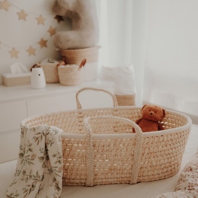 Berço de bebé em cesto de palha com ursinho de peluche e pano floral num quarto decorado em tons claros