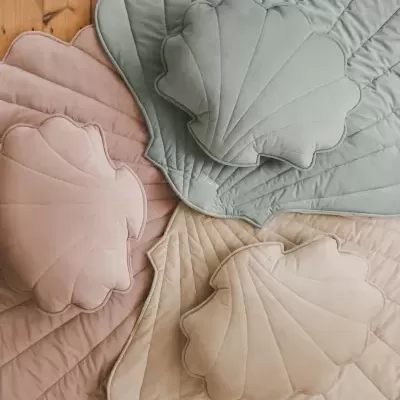 Almofadas e colchas em forma de concha em tons pastel sobre chão de madeira