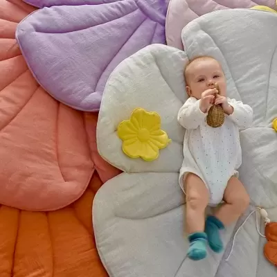 Bebé deitado em tapetes almofadados coloridos em forma de pétalas de flores