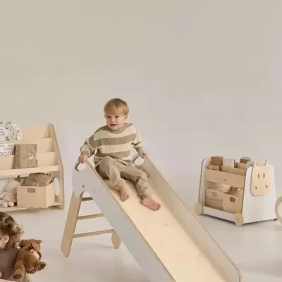 Criança num escorrega de madeira clara com laterais brancas, sala com móveis de madeira clara e armazenamento branco