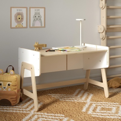 Secretária infantil em madeira clara e branca com gavetas, tapete bege, mochila tigre e quadros na parede