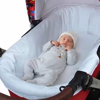 Bebé vestido num macacão cinzento claro a dormir num carrinho branco e vermelho