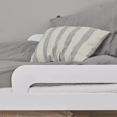 Cama branca com roupa de cama cinzenta e almofada riscada bege e azul