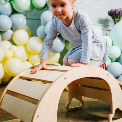 Menina a brincar com brinquedo de madeira claro e balões coloridos pastel em fundo