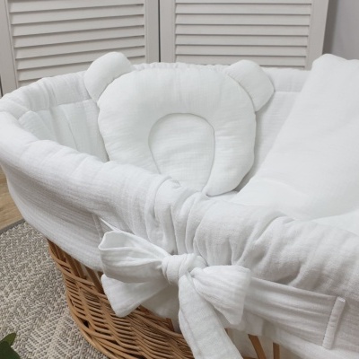 Berço de vime com forro branco e almofada de urso em ambiente interior