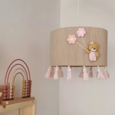 Candeeiro de teto redondo com ursinho e balões cor-de-rosa, suspenso num quarto branco com prateleira de madeira e brinquedo colorido.