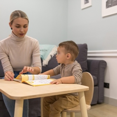 Mesa e cadeira de madeira clara numa sala com sofá cinzento e parede azul clara