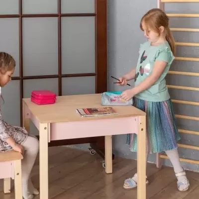 Conjunto de mesa e bancos infantis em madeira clara com dois estojos coloridos sobre a mesa