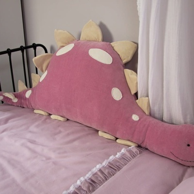 Almofada dinossauro cor-de-rosa numa cama com lençóis cor-de-rosa claro