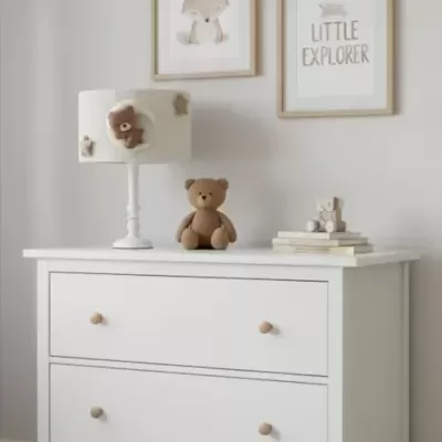 Cómoda branca de madeira com abajur decorado, urso de peluche e quadros na parede