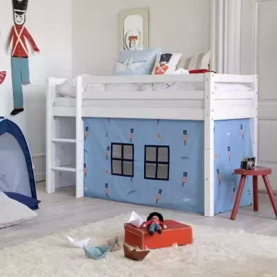 Cama alta branca com tecido azul decorado com soldados e janelas, almofadas, tapete peludo branco e brinquedos