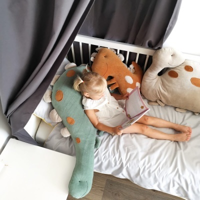 Criança a ler no berço com almofadas de dinossauro coloridas