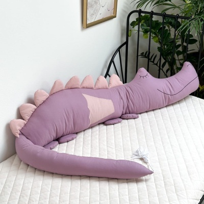 Almofada decorativa em forma de crocodilo cor de rosa sobre colchão branco.