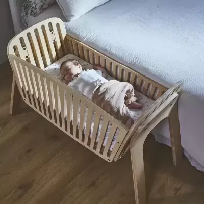 Berço de madeira clara com bebé a dormir, ao lado de cama branca