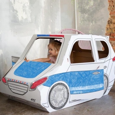 Carrinho de brinquedo em cartão azul e branco em forma de carro de polícia, com criança dentro