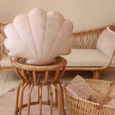 Cadeira rosa em forma de concha com estrutura de vime numa sala com sofá e cesto de vime