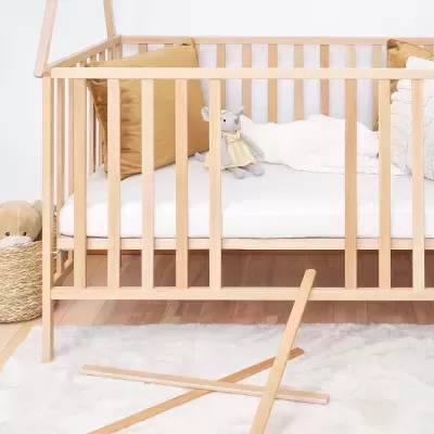 Berço de madeira clara com colchão branco e almofadas castanhas