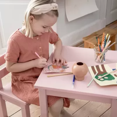Menina desenhando numa mesa cor-de-rosa com lápis de cor e canetas