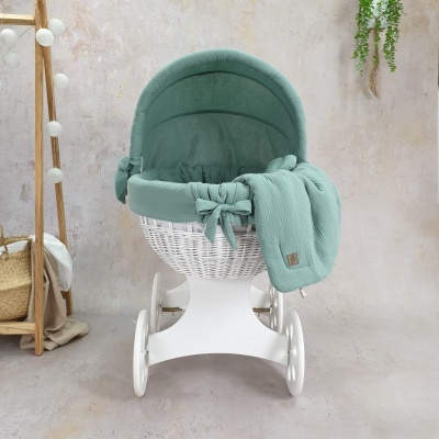 Berço de bebé em vime branco com acolchoado verde água num ambiente interior claro