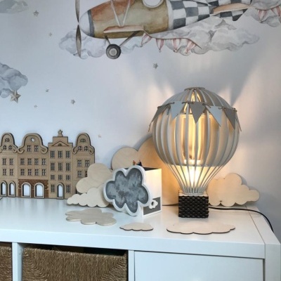 Abajur de madeira em forma de balão com decoração de estrelas, nuvens decorativas, e parede com desenho de avião antigo com padrão xadrez