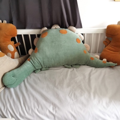 Peluches de dinossauros em cama com lençol cinzento e cortina cinzenta ao fundo