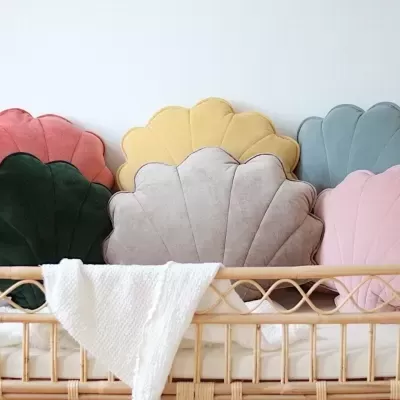 Seis almofadas coloridas em forma de concha numa cama de vime