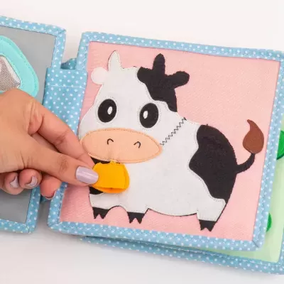 Livro de tecido com vaca em página cor-de-rosa e borda azul