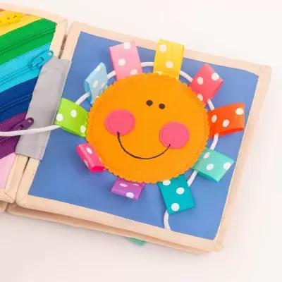 Livro de pano colorido para bebés com um sol sorridente e fitas coloridas