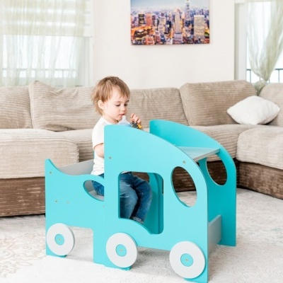 Criança sentada em brinquedo de madeira azul claro em forma de carro numa sala com sofá castanho claro