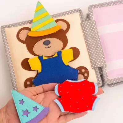 Livro de tecido com urso castanho e roupa infantil colorida