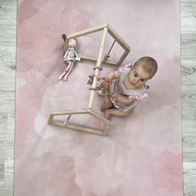 Tapete de brincar rosa com criança, brinquedo de madeira e boneca de pano