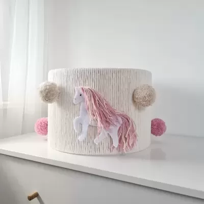 Decoração infantil redonda branca com pompons e unicórnio rosa, sobre uma superfície branca