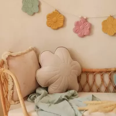 Sofá rattan com almofada creme em forma de flor, manta verde e decoração floral colorida na parede