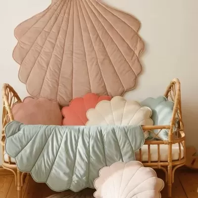 Conjunto de almofadas e tapetes em forma de concha em tons pastel num berço de vime