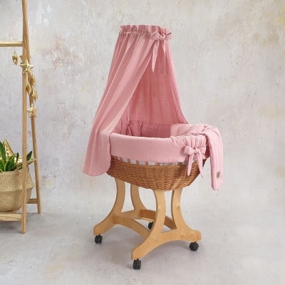 Berço de bebé em madeira clara com tecido rosa e dossel, em ambiente interior minimalista