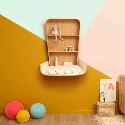 Estante de madeira clara com boneca, cogumelos e frasco, parede colorida em triângulos e bolas de tecido no chão