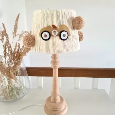 Candeeiro de mesa com base de madeira clara e cúpula creme decorada com apliques redondos em padrão de olhos