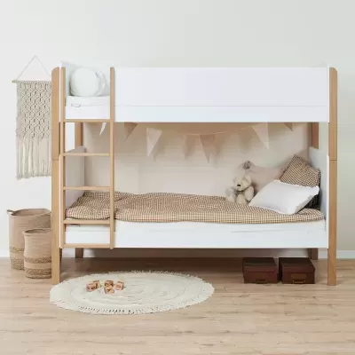 Cama de beliche branca e madeira com roupa de cama xadrez e almofadas, tapete circular e cestos de corda.