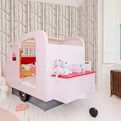 Quarto infantil com cama caravana cor-de-rosa, figuras de coelho e papel de parede troncos